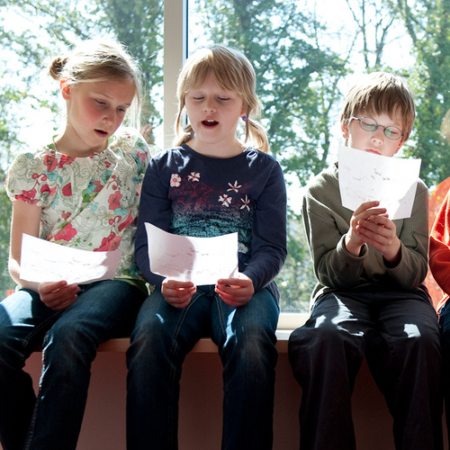 Vier Kinder sitzen auf eine Fensterbank und singen nach Noten